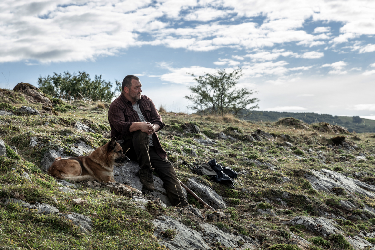 Antoine (Denis Ménochet) seduto su un’altura insieme al suo cane, osserva il paesaggio rurale.