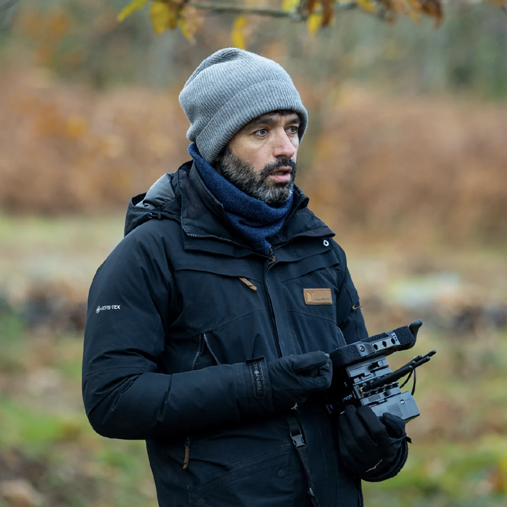 Il regista Rodrigo Sorogoyen sul set di As Bestas, vestito con abiti invernali e berretto, mentre tiene in mano una macchina da presa.