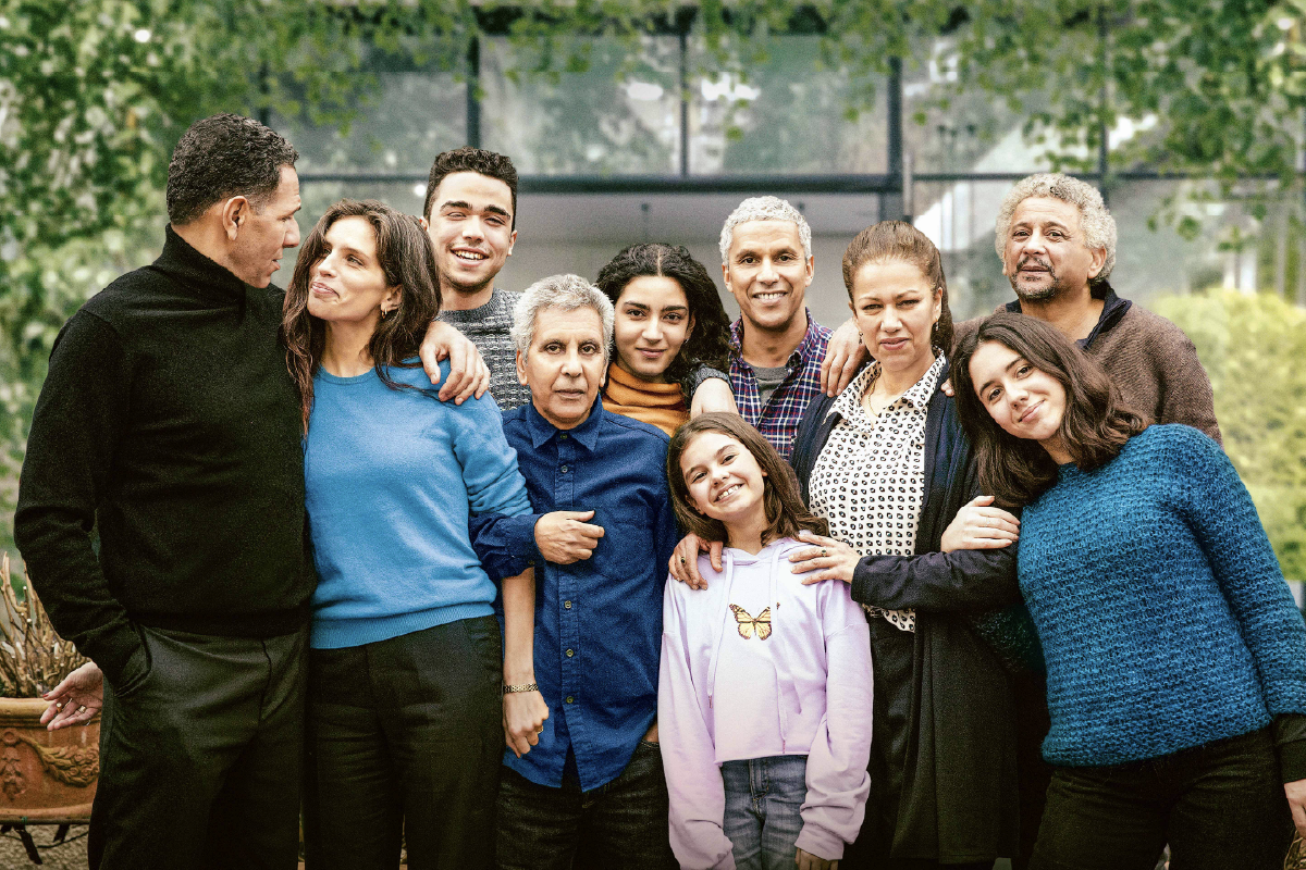I protagonisti del film Ritratto di Famiglia posano tutti insieme davanti a una casa immersa nel verde, sorridenti e affiatati, in un ritratto corale.