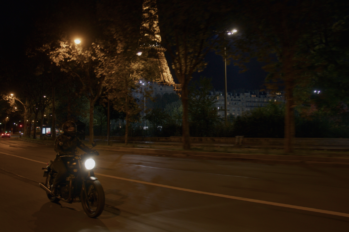 Un motociclista attraversa Parigi sotto la Tour Eiffel illuminata, in una delle sequenze notturne del film Riabbracciare Parigi.